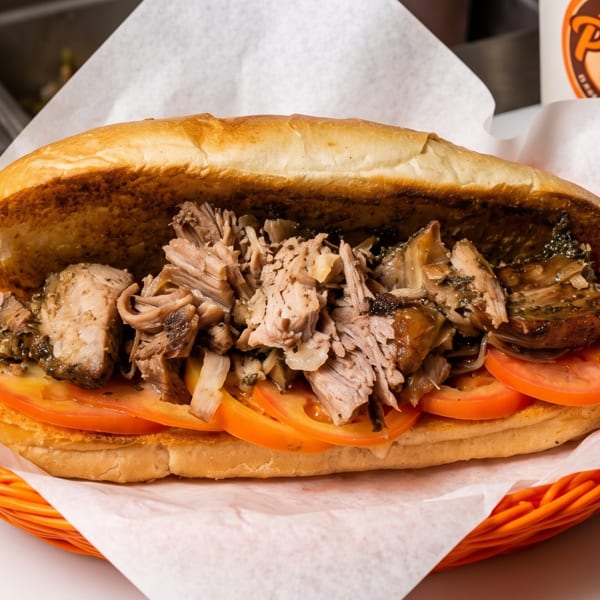 A Porky's Pork Belly sandwich with shredded pork and sliced tomatoes in an orange basket.