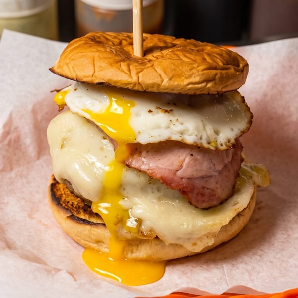 A breakfast sandwich with ham, melted cheese, and a fried egg with a runny yolk, served in an orange basket.