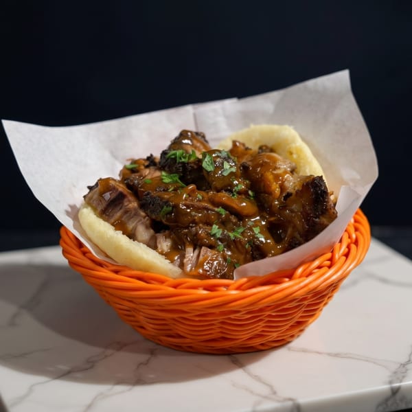 Arepa filled with saucy shredded beef and mushrooms, garnished with parsley, in an orange basket.